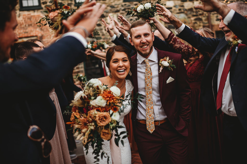 Baltimore wedding photographers captures bride and groom holding hands and running through their bridal party as they raise their hands over the couples head