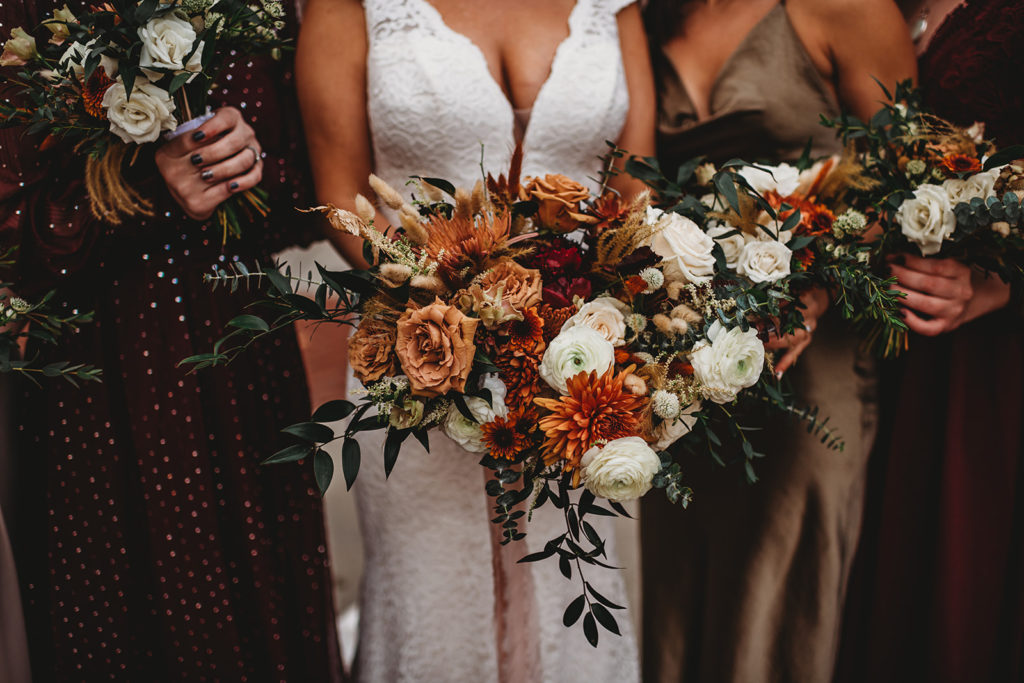 bride holding a warm tone floral bouquet while standing with her bridesmaids who are in fall bridesmaids dresses captured by Baltimore wedding photographer 