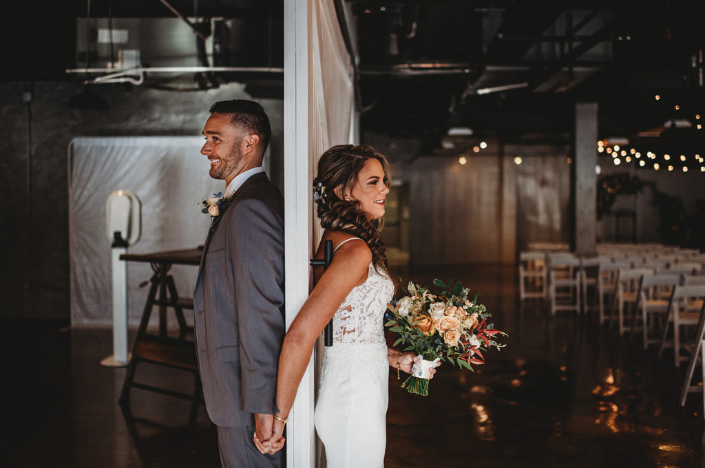 bride and groom standing on opposite sides of a door together and holding hands for their first touch photographed by Maryland wedding photographer 