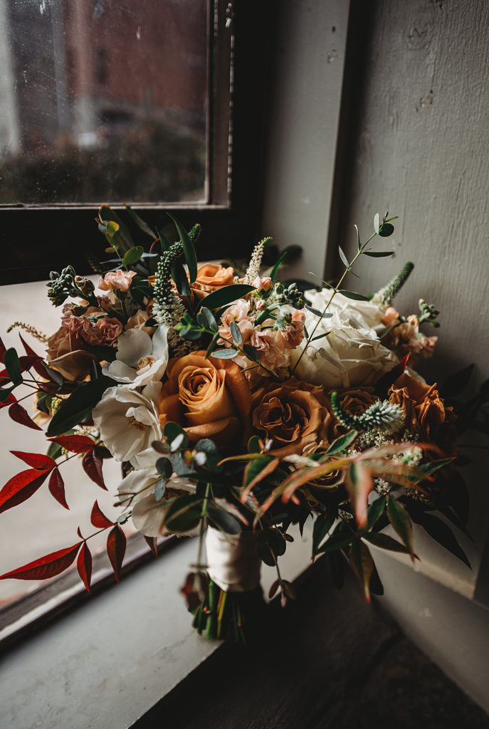 bridal bouquet with rust florals and sage greens sitting in a window captured by Baltimore wedding photographers