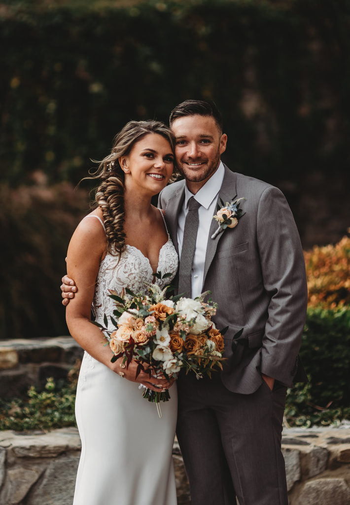 Baltimore wedding photographer captures bride and groom standing close together and posing as the bride in a lace wedding dress holding a large floral bouquet 