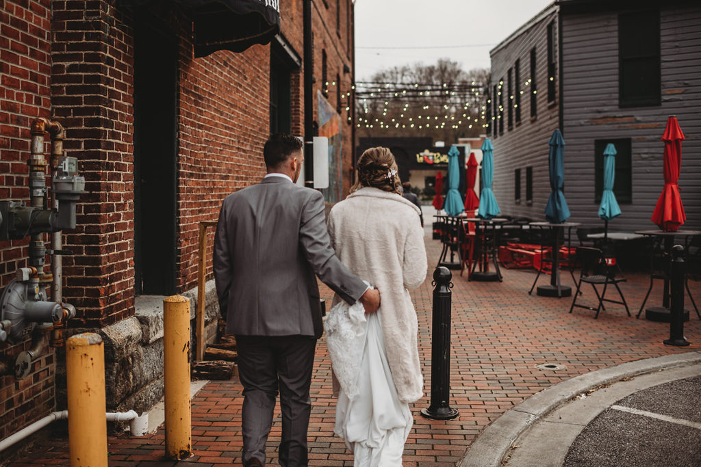 Maryland wedding photographer captures bride and groom walking through historic Ellicott City while the groom holds the brides wedding train 