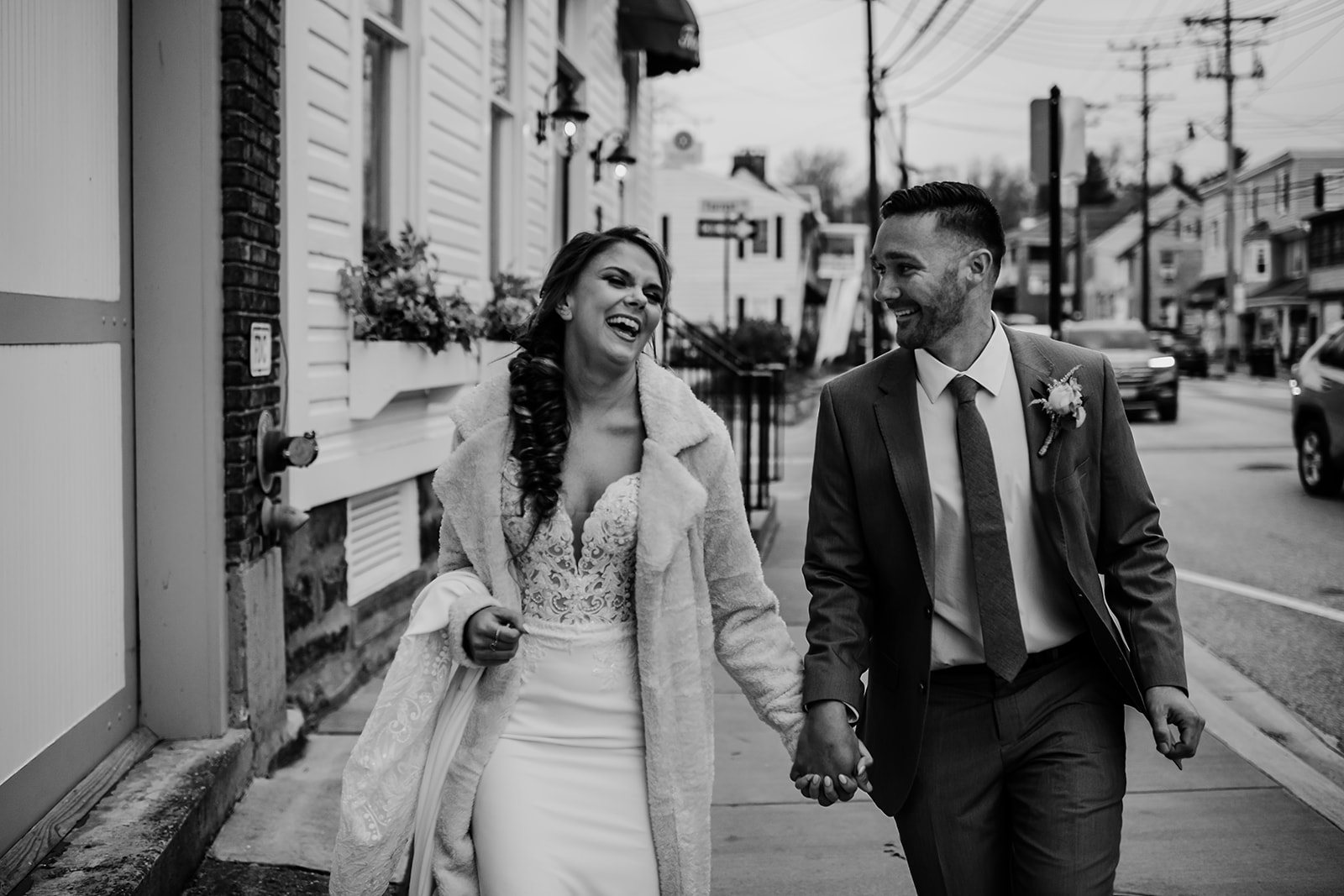 Baltimore wedding with bride and groom holding hands and walking down a sidewalk in downtown as they laugh together captured by Baltimore wedding photographers
