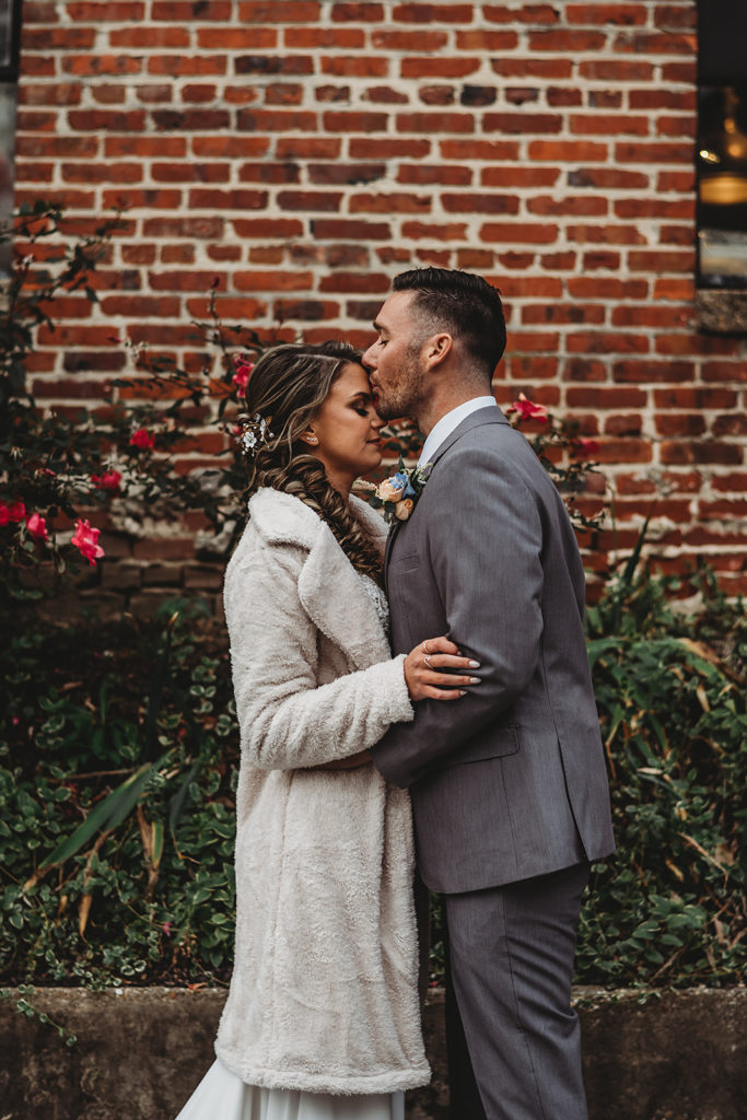 bridal portraits by Baltimore wedding photographers with bride in a faux fur coat facing her groom and holding his arms as he leans in and kisses her forehead