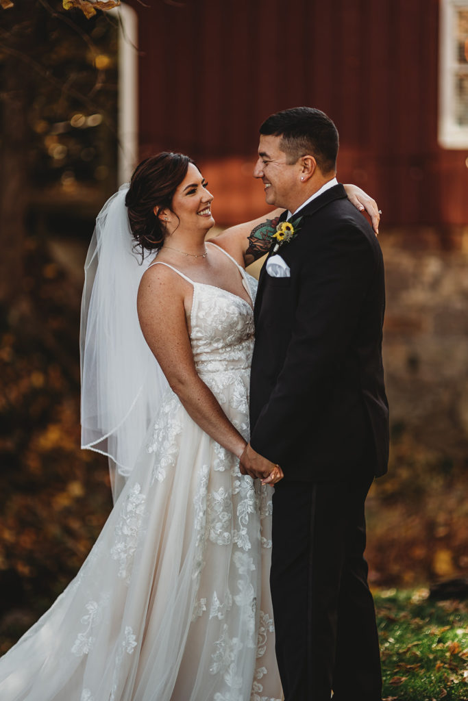 bride and groom standing close and holding hands as the bride leans back to look at her groom and smiles at him joyfully captured by Baltimore wedding photographers
