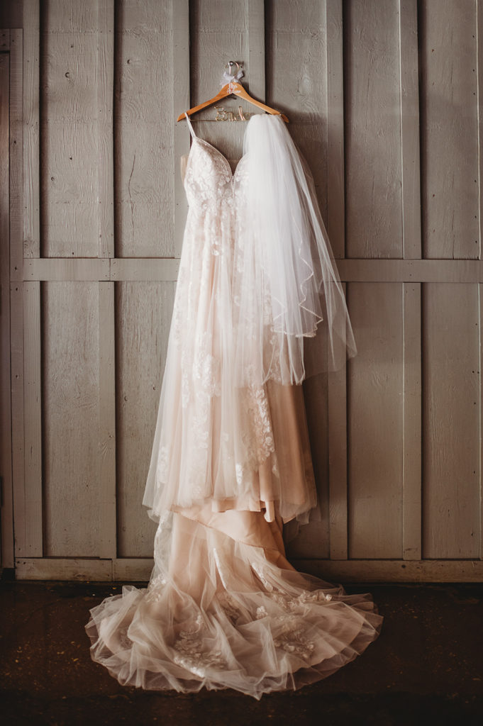 Baltimore wedding photographers capture lace wedding dress hanging on a door frame with the brides veil draped over part of the hanger in a bridal suite at Baltimore wedding venue 