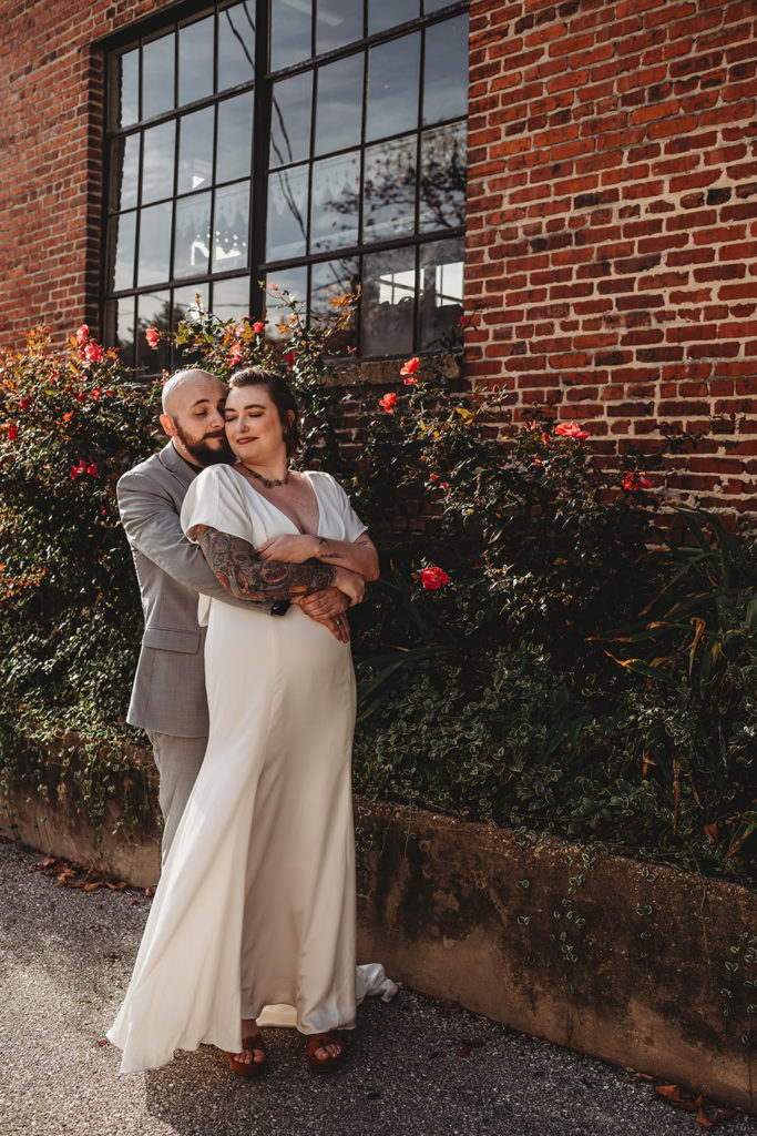 Maryland wedding photographer photographs bride and groom embracing next to a rose bush in a downtown street