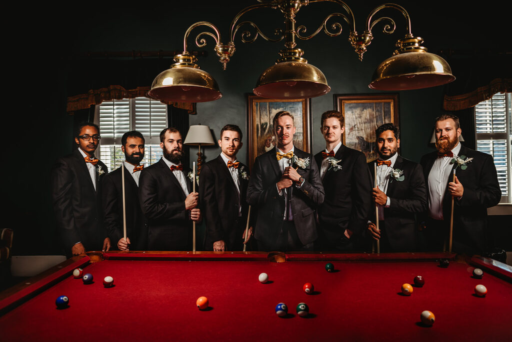 groom and his groomsmen standing at a pool table for wedding pictures by Baltimore photographers