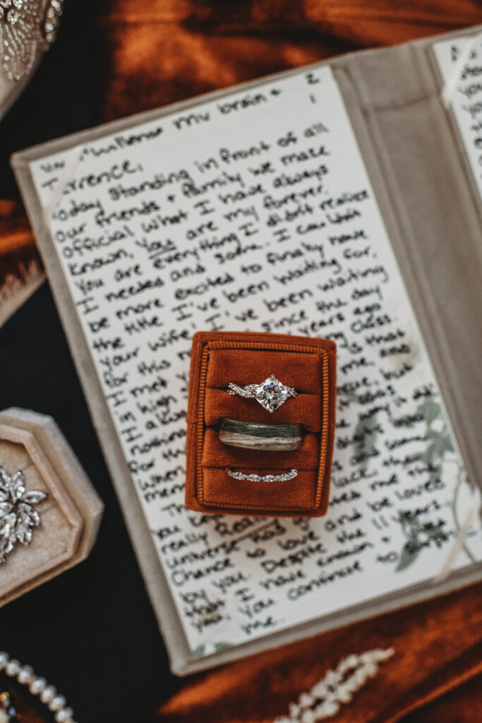Engagement ring and wedding band and a orange box on top of a letter for wedding detail shots by Baltimore photographers