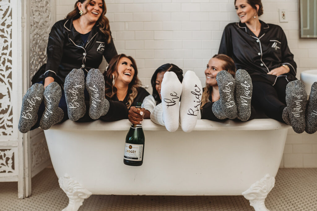 Bride and her bridesmaids sitting in a claw tub while drinking champagne together before the wedding ceremony photographed by Baltimore photographers