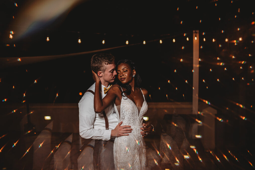 Baltimore photographers captures bride and groom dancing at their reception with twinkle lights overhead  with bride holding her grooms cheek as they embrace one another