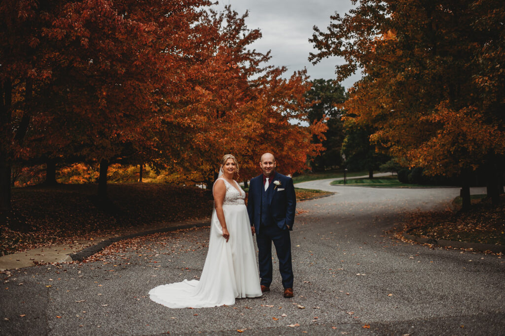 bride and groom standing in a road with autumn trees surrounding them for their outdoor wedding portraits with Maryland wedding photographer