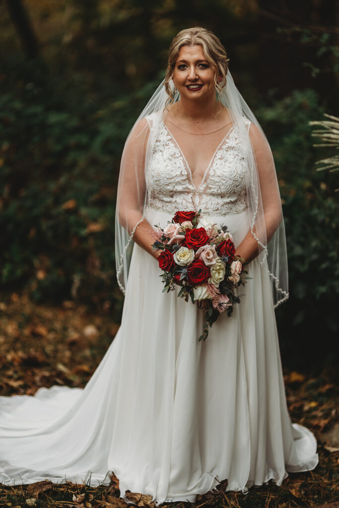 Baltimore wedding photographer captures bridal portrait with bride in a lace wedding gown holding a red rose bouquet in a garden at a Baltimore wedding venue