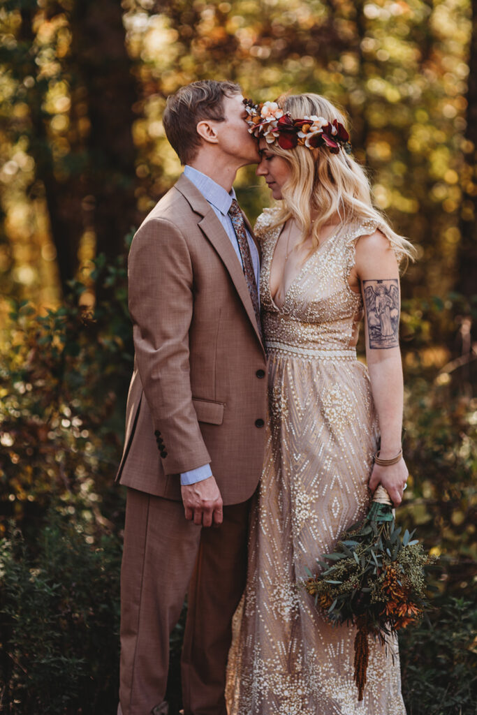 groom kissing his bride on the forehead as they stand in the woods for their outdoor Baltimore wedding with Maryland photographer 