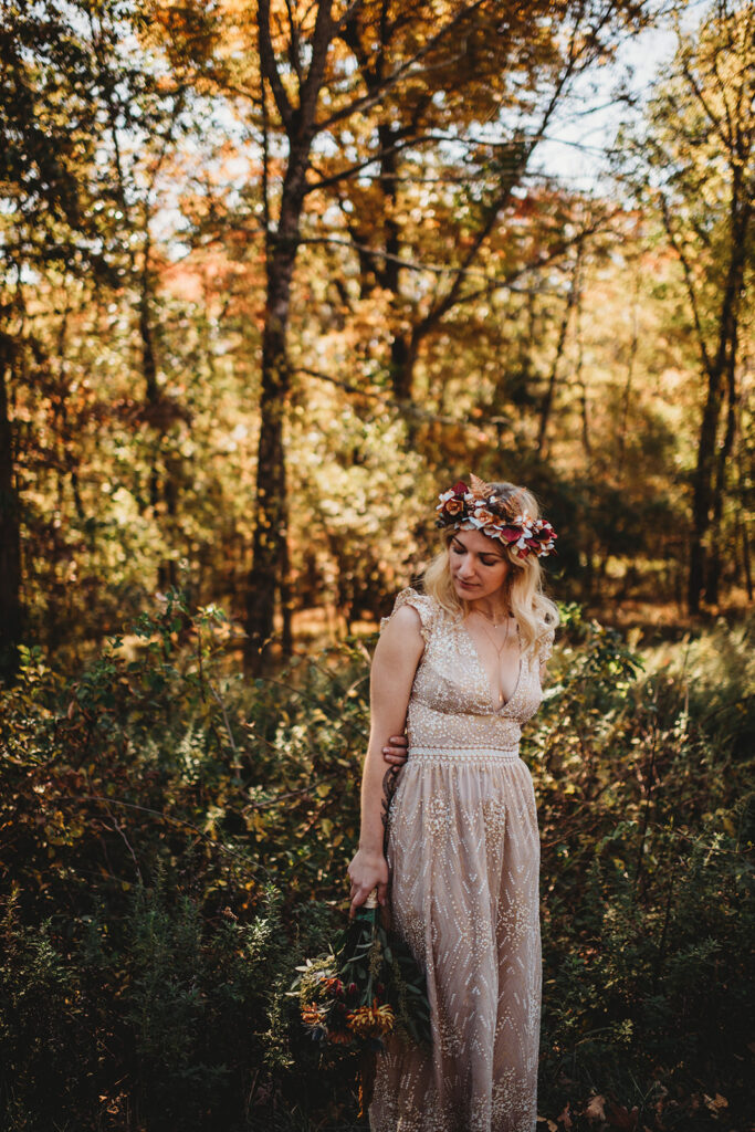 bridal photoshoot with bride in a lace dress walking through the woods in the fall while holding her bouquet to her side captured by Maryland wedding photographer