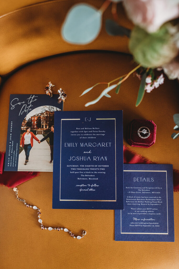 Baltimore wedding photos of wedding invitations that are a dark blue with gold details on an orange couch with red ribbon behind the invites