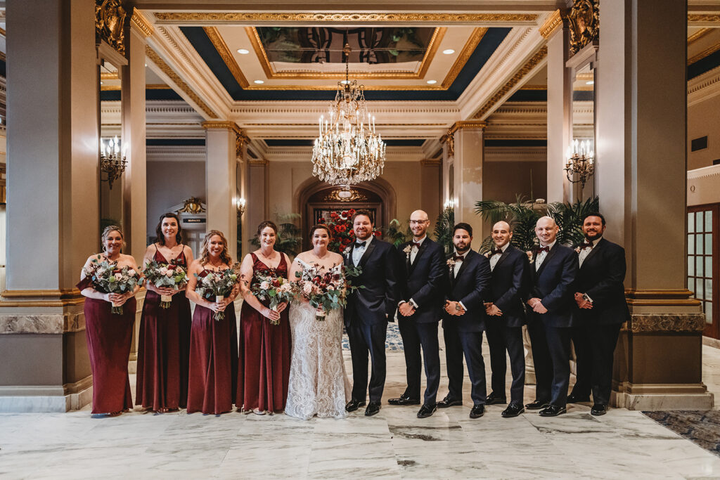 bride and groom groom posing together in a grand foyer with their bridal party all standing together captured by Baltimore photographers