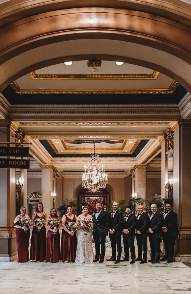 bridal party with bride and groom standing in the middle of a large foyer with the groomsmen to one side and the bridesmaids to the other at the Belvedere wedding venue
