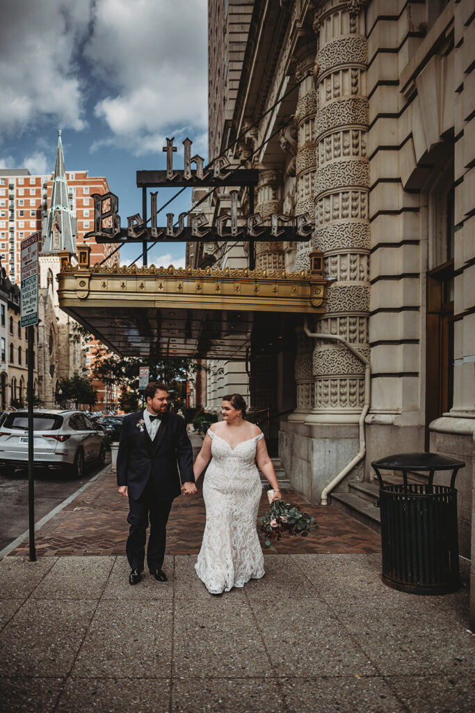 Baltimore photographers photographs outdoor wedding pictures with bride and groom holding hands and walking down a side walk together outside of the Belvedere wedding venue