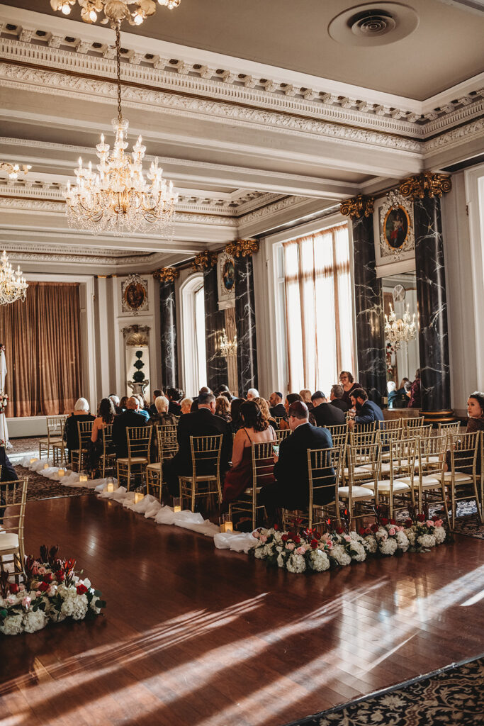 the belvedere wedding venue ceremony hall with golden chairs and guests watching the ceremony captured by Baltimore photographers