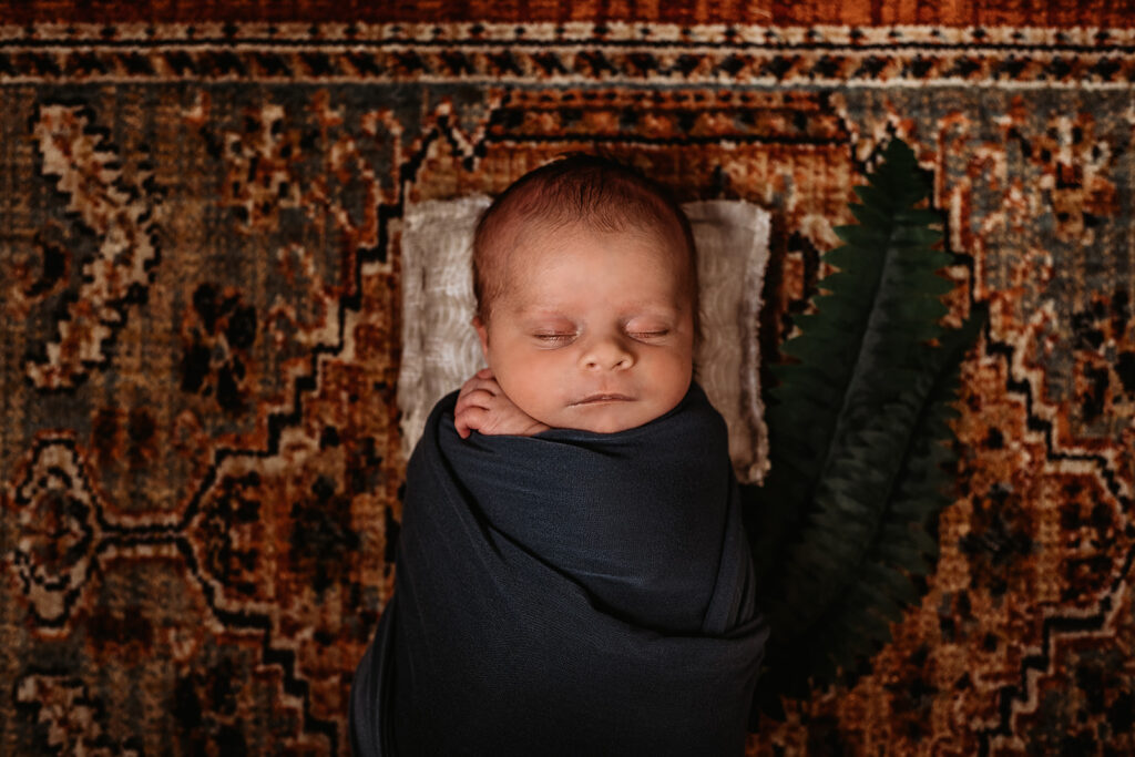 newborn photography with baby in a dark blue swaddle laying on a Moroccan rug while sleeping