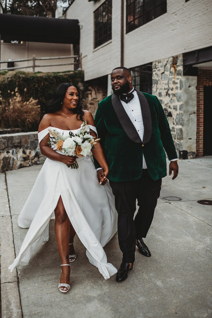 Baltimore photographers captures bride and groom holding hands and walking together as the wind blows the brides skirt through her slip while her groom chats with her