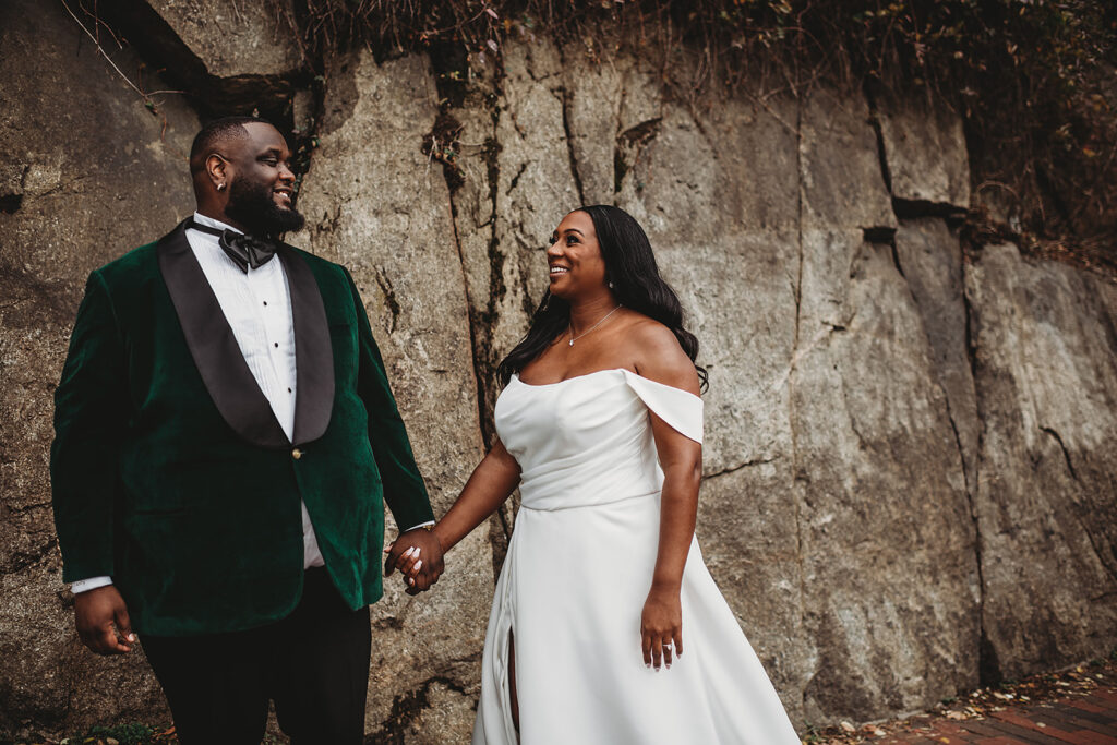 Maryland wedding photographer photographs bride and groom holding hands as the bride looks up and smiles at her groom who is wearing a emerald green suit 