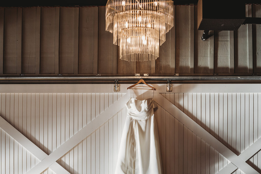 brides satin wedding dress hanging on a barn door at a Baltimore wedding venue photographed by Maryland wedding photographer