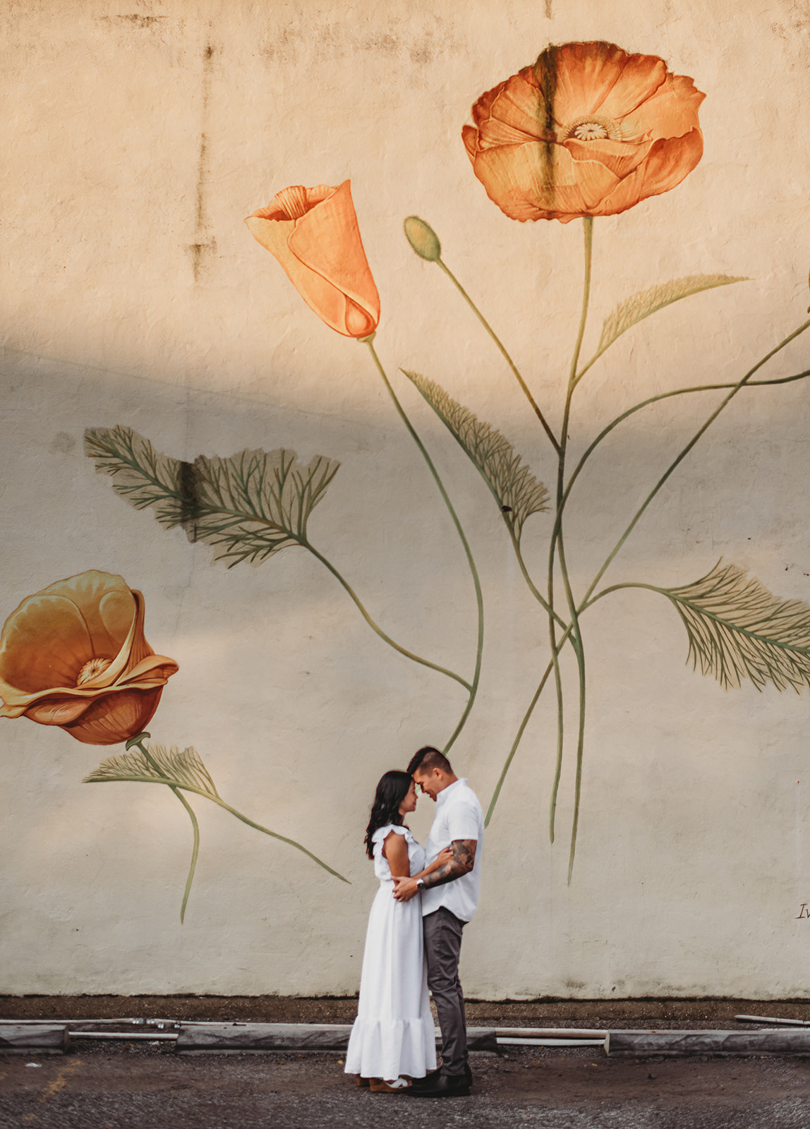 downtown engagement session in Georgetown Washington DC with man in a white shirt and dark pant holding a woman in a long white dress in front of a large wall art mural of boho florals