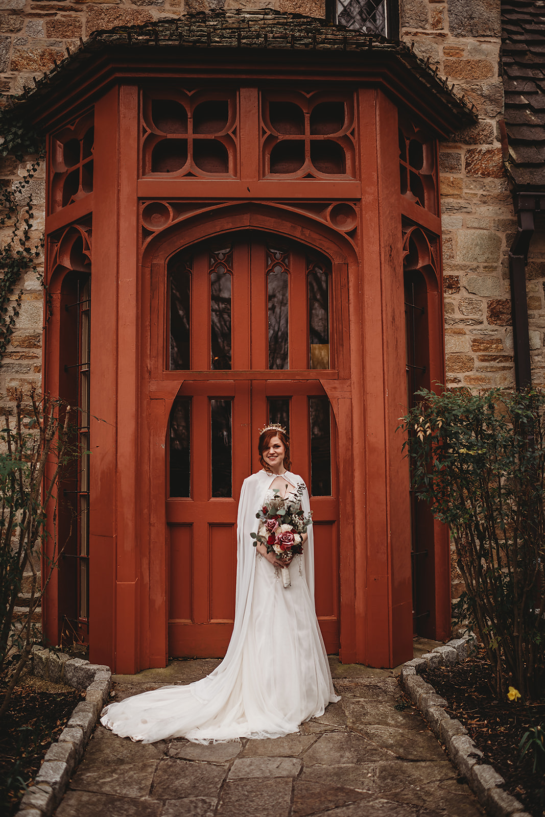 bride standing outside of a red door at The Cloisters Castle wedding venue in Maryland and posing for her bridal portraits