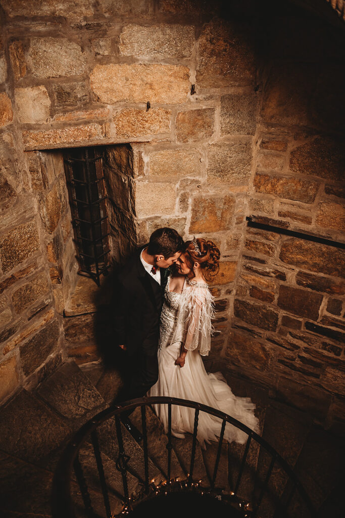 bride and groom standing in a stairwell of a castle with stone walls and little lighting captured by Baltimore photographers