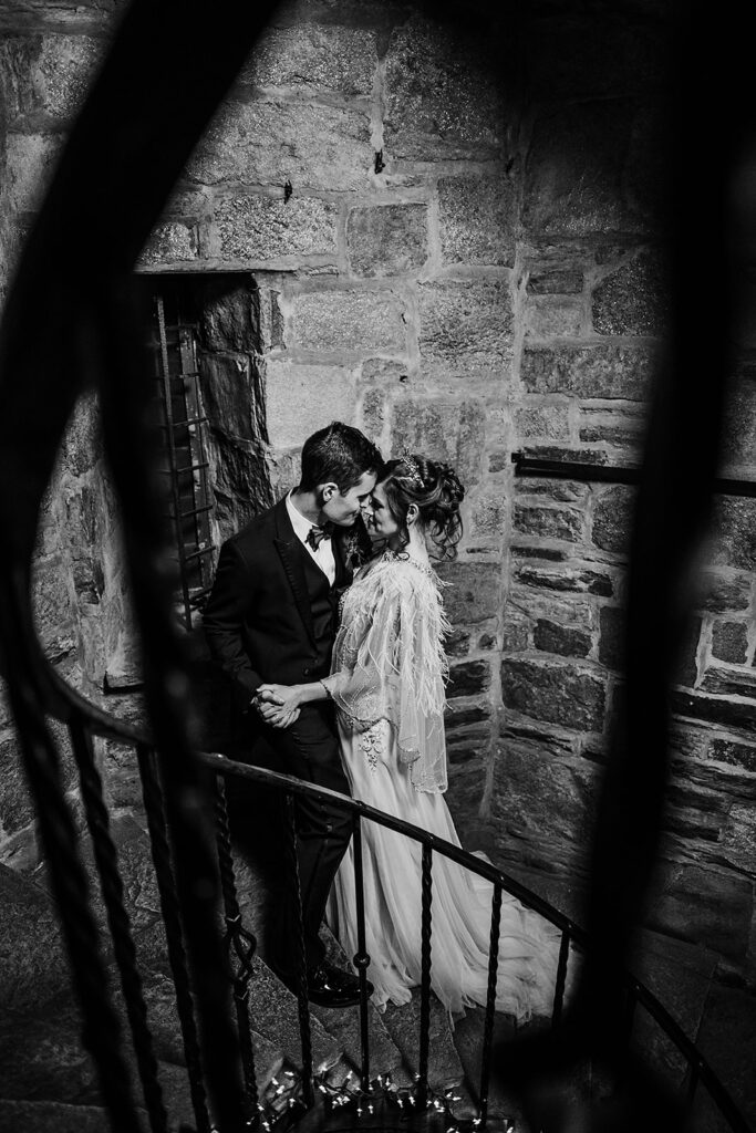 black and white bridal portraits by Baltimore wedding photographers with bride and groom standing on a spiral stair case with the groom holding his brides waist as she leans into him and rests her forehead against his lips