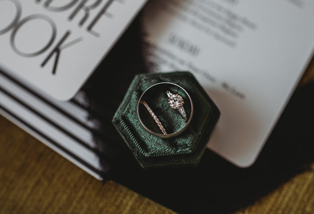 Brides engagement ring and wedding band in a dark green ring box with the grooms ring o top of the brides captured for Baltimore wedding photos