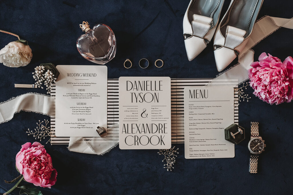 Baltimore wedding photographers captures a flatlay on a dark blue background with bright pink florals and white invitation and small details 