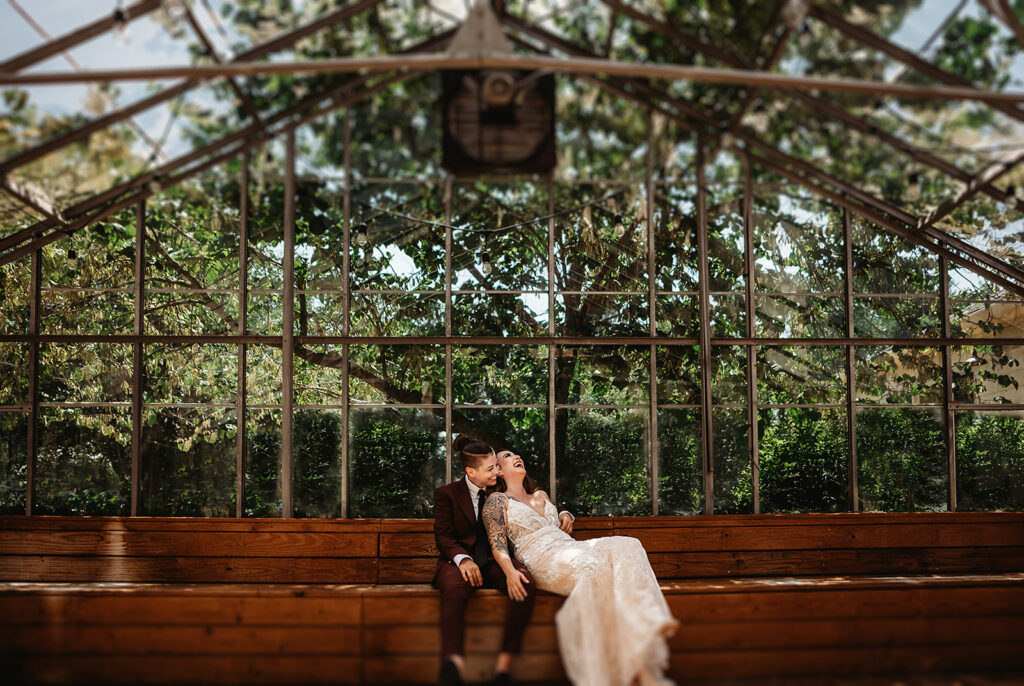 lgbtq wedding with couple sitting on a bench in a greenhouse cuddling for their bridal portraits with 
Baltimore wedding photographers