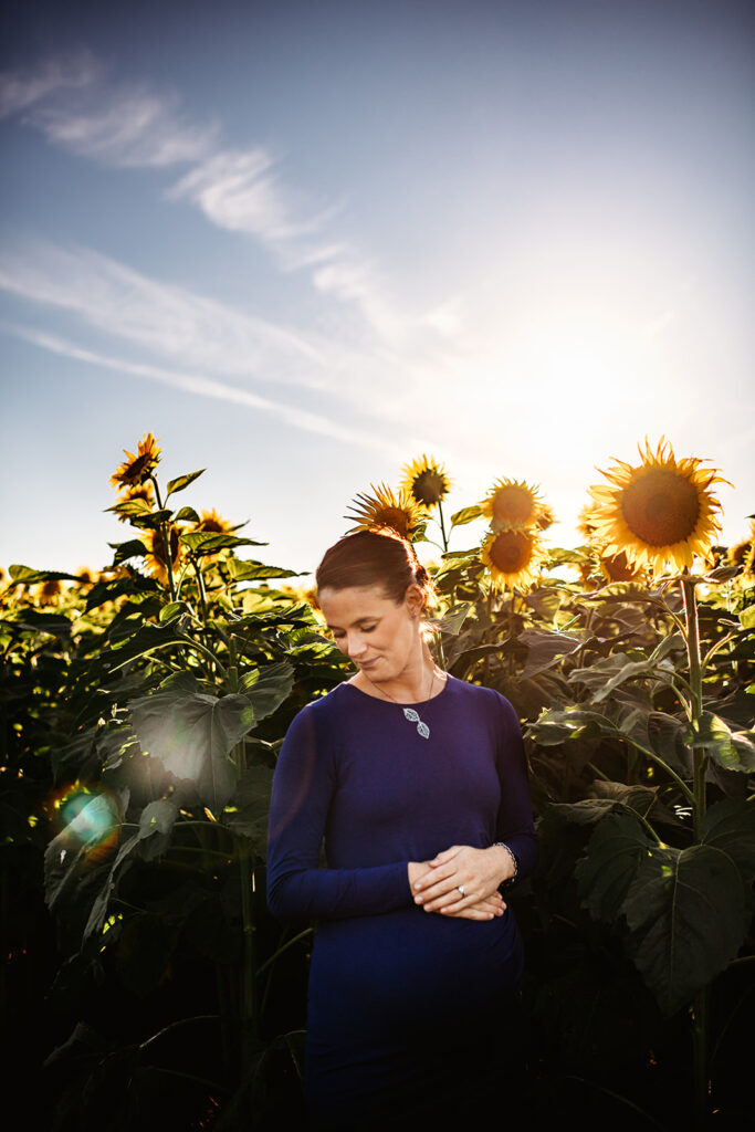 Baltimore photographers capture pregnant mama standing in sunflower field wearing blue dress