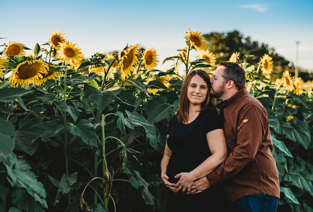 Baltimore photographers capture man holding woman's belly during maternity photos in sunflower field