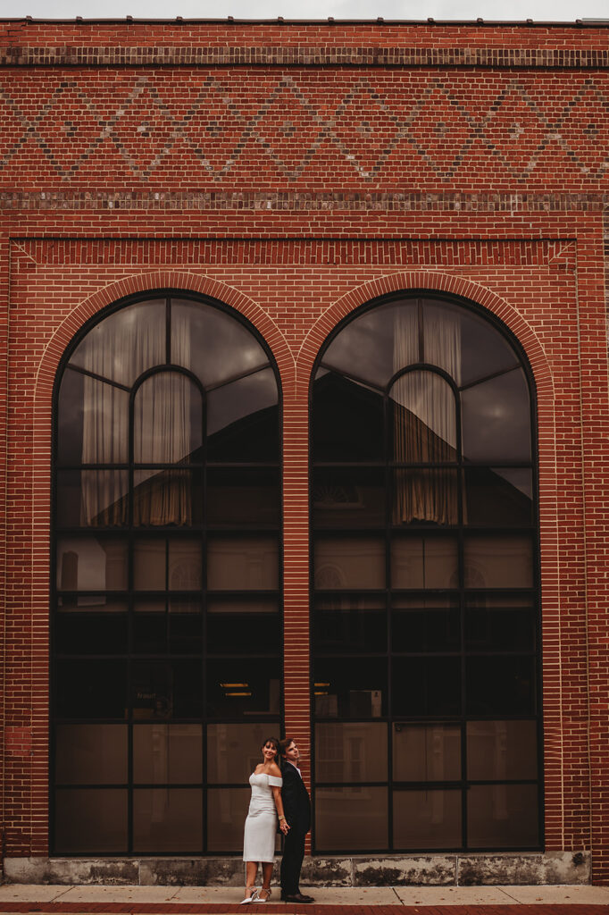 Maryland engagement photographers captures couple standing in front of brick building 