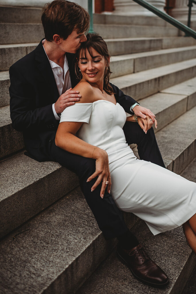 Maryland engagement photographers capture woman wearing white dress and man wearing suit sitting on stairs