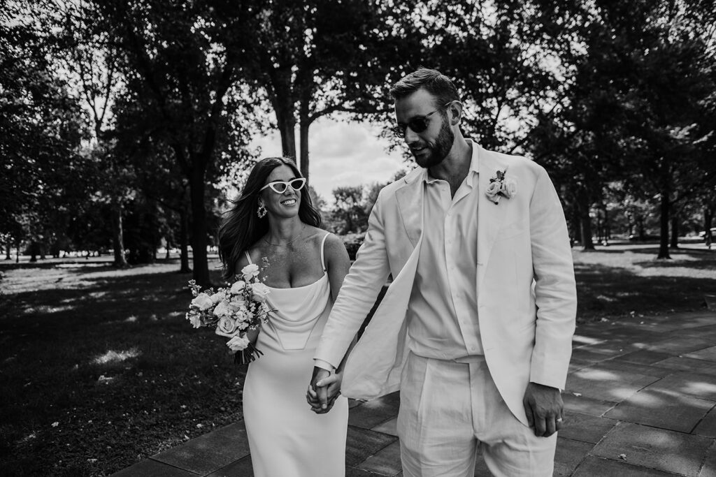 Baltimore wedding photographer captures couple walking hand in hand wearing sunglasses after War Memorial Wedding