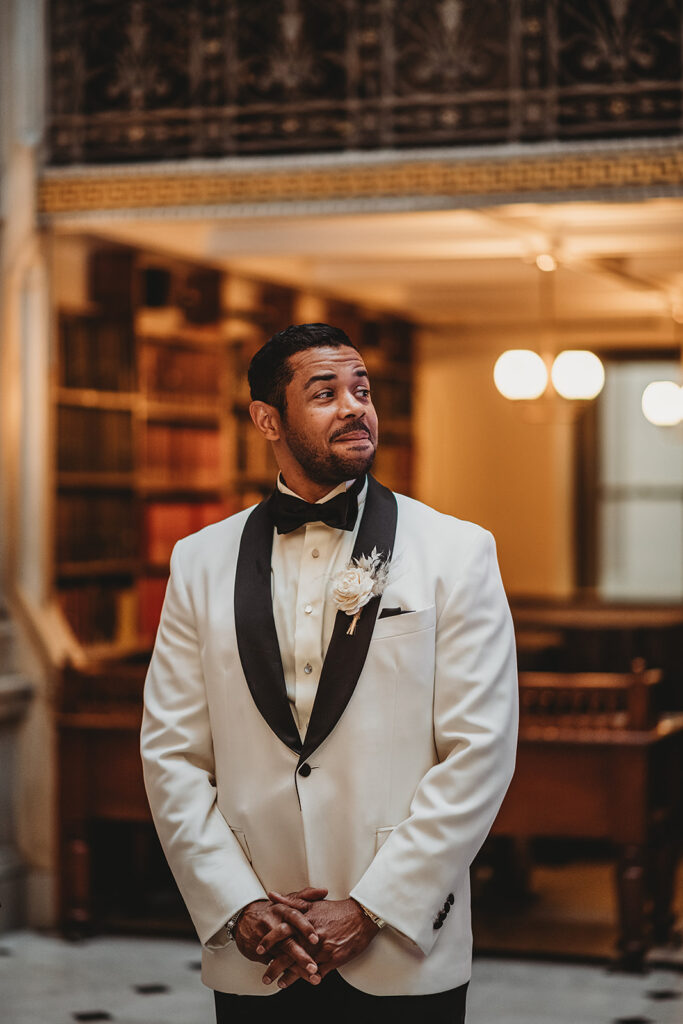 Baltimore wedding photographer captures groom wearing white suit watching bride walking down the aisle at Baltimore Library wedding