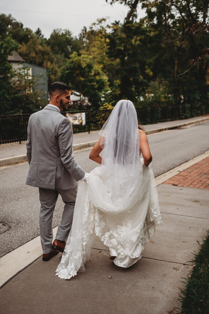 Maryland wedding photographer captures groom holding bride's train while walking