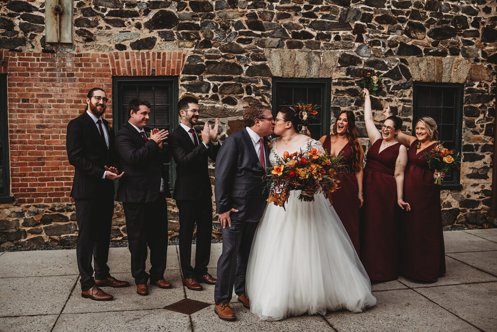 Baltimore wedding photographer captures bride and groom kissing while wedding party celebrates