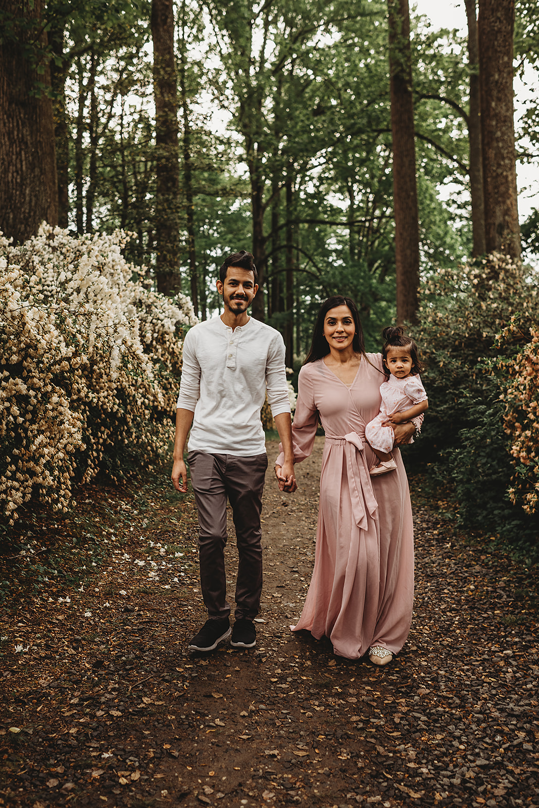 man and woman holding hands and walking on a trail together while the mother holds their little girl with lush woods behind him captured by Baltimore photographers