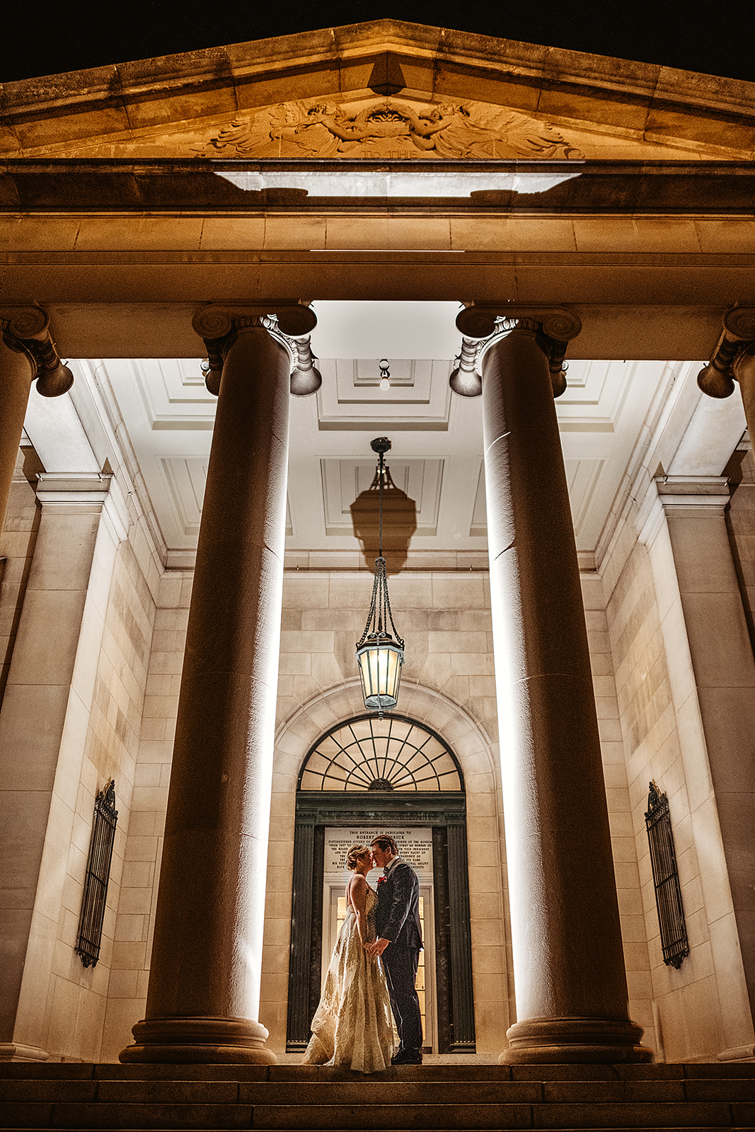 outdoor wedding photos at the Baltimore Museum of Art with bride and groom kissing under the porch lights with large pillars on either side of them