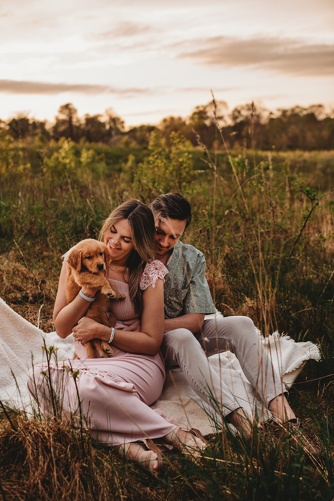 Howard County Conservatory photos with couple sitting on a blanket holding a puppy at sunset with pink clouds overhead behind them