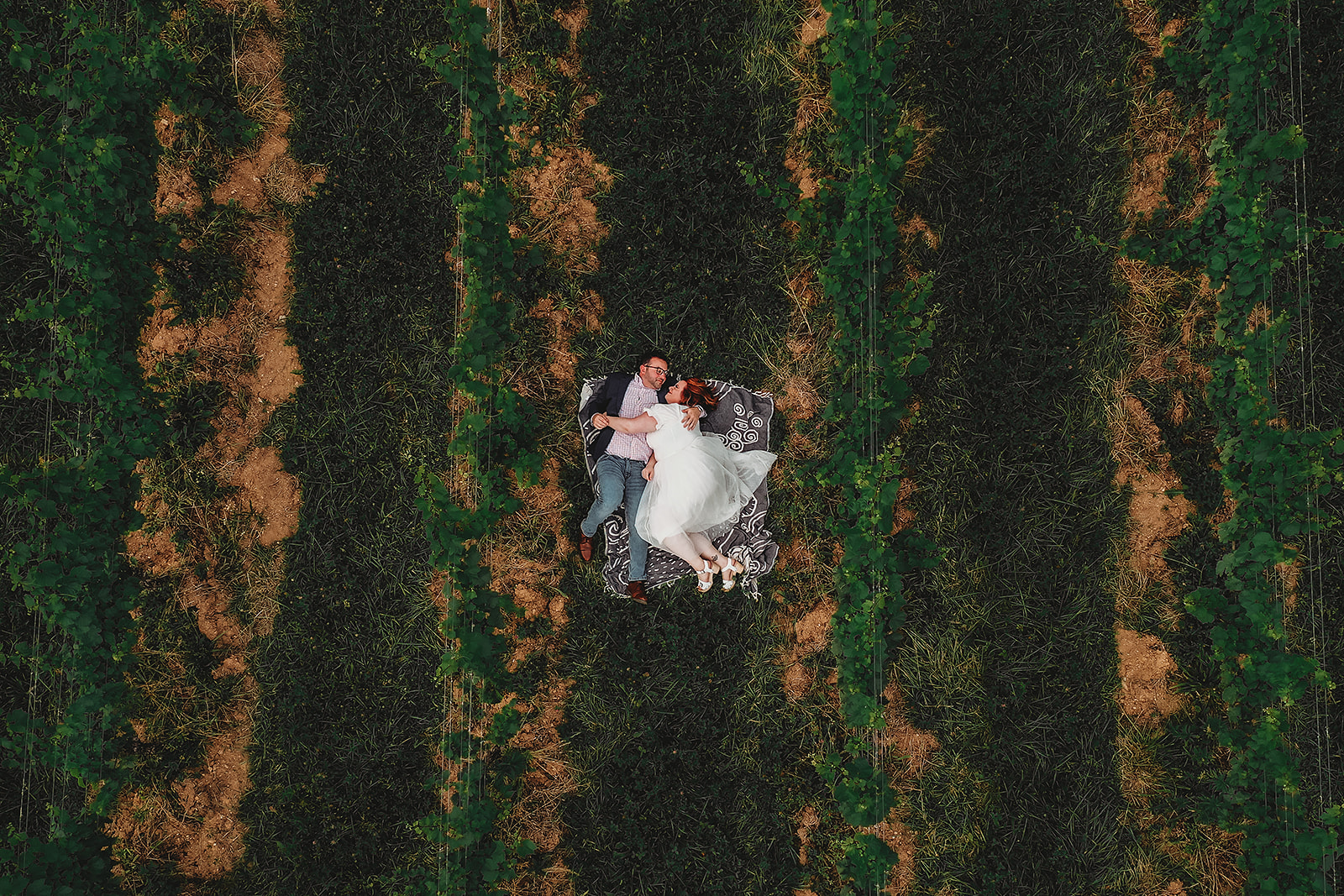 man and woman lay on a silk lace blanket in the middle of a wine vineyard in Baltimore for engagement photos