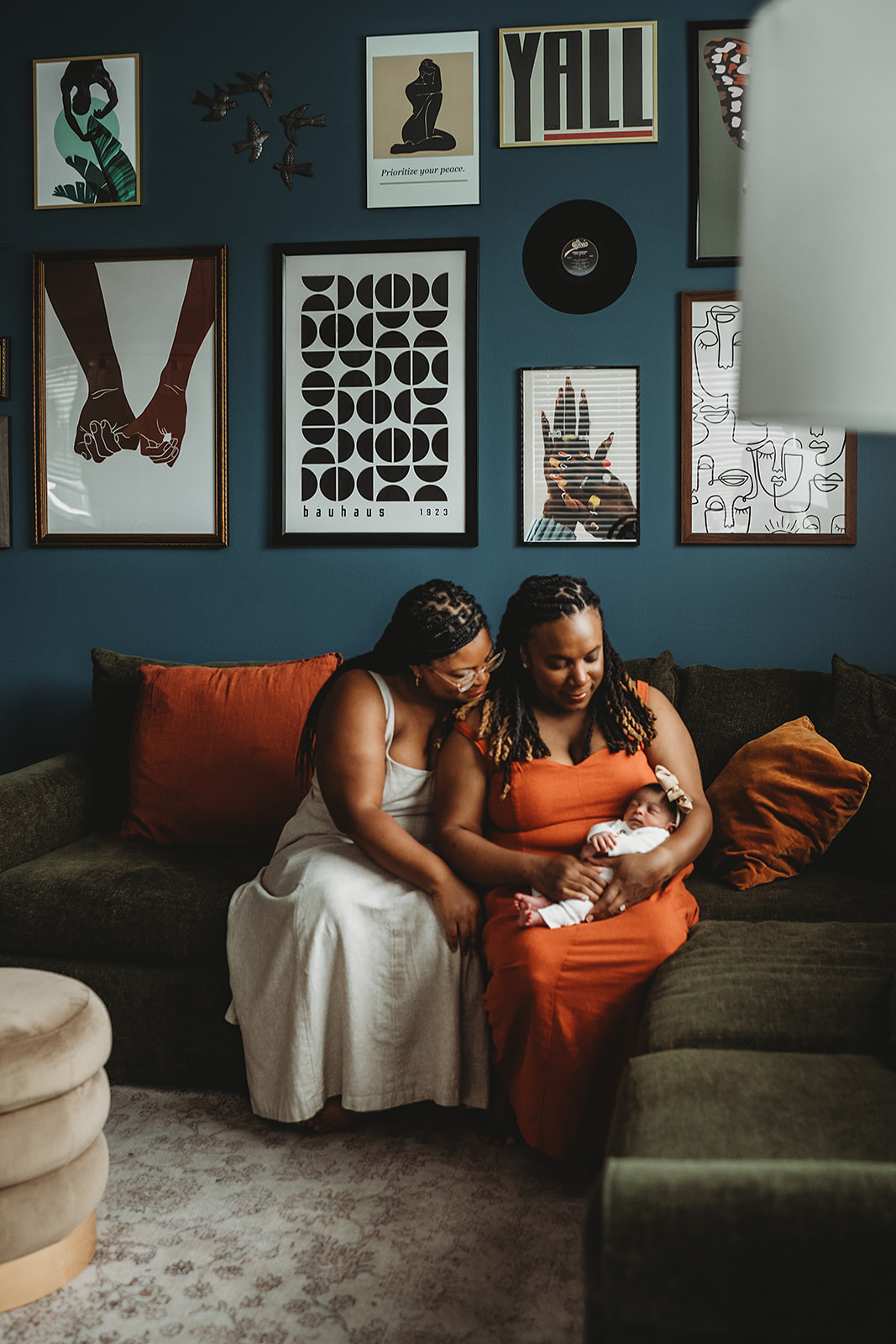 newborn pictures at home with lesbian couple sitting on a couch in their living room while they hold their newborn baby