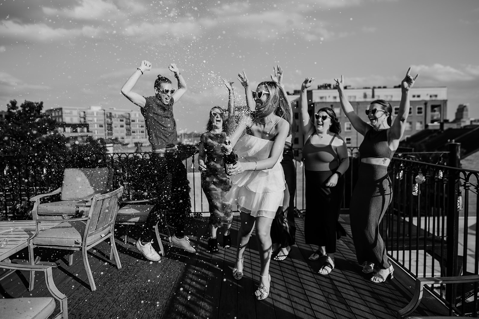 black and white bachelorette party photo taken by baltmiore wedding photographer with bride popping champagne on a rooftop with her bridesmaids