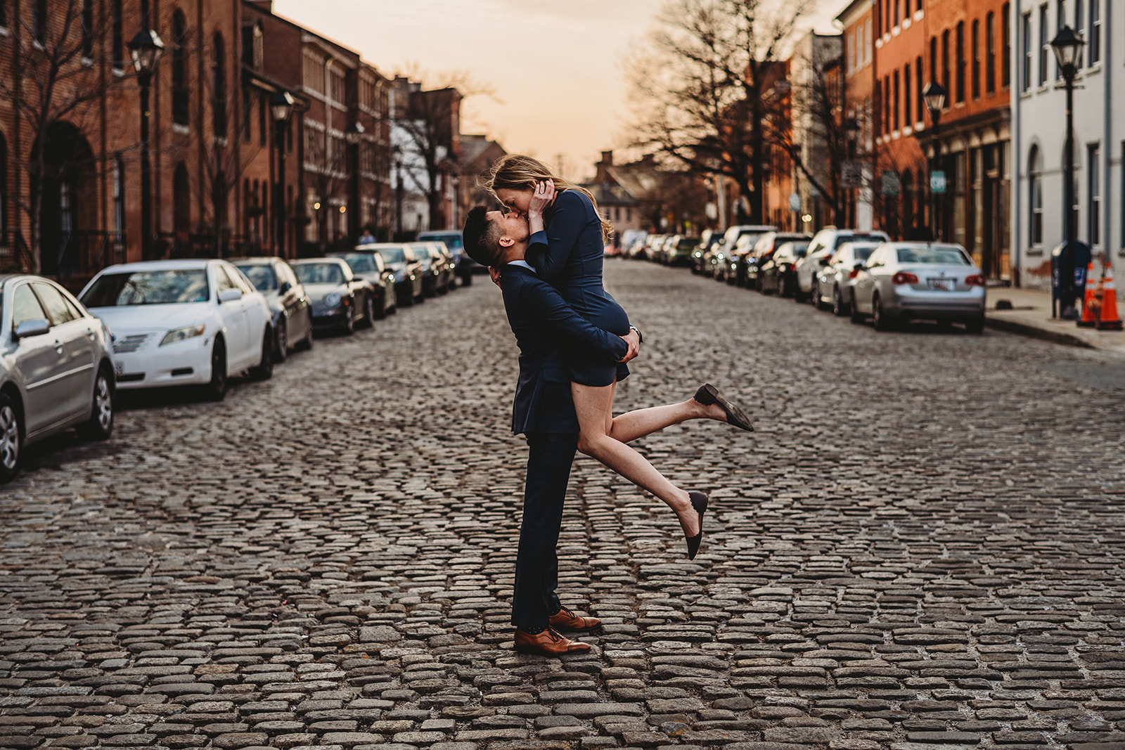 couples photography by Baltimore wedding photographer with man picking up woman as they kiss and she kicks up her legs in the middle of a cobblestone road